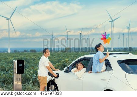 Concept Of Progressive Happy Family Enjoying Their Time At Wind Farm With Electric Vehicle. Electric