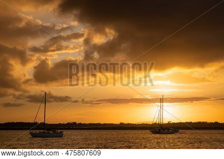 Sunset With Orange Sky Over Two Silhouetted Yachts On The Clarence River In Australia