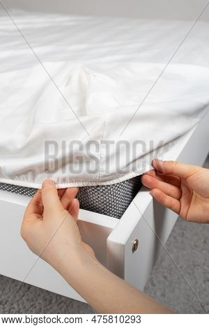 A White Satin Sheet With An Elastic Band Is Put On The Mattress Of The Bed, A Close-up Of The Hands.