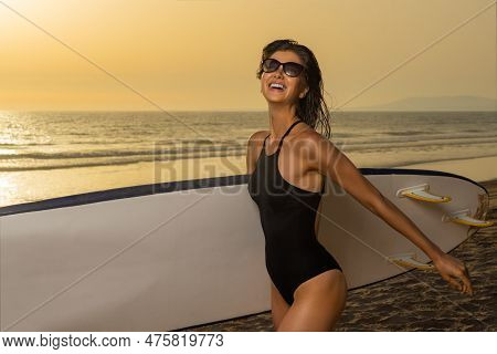 Smiling Girl With Surf Board Ready To Surfing. Woman Surfer Holding Surfboard On A Beach At Sunset O