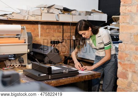 Busy Typographer Holding Knife Near Paper While Working In Print Center.