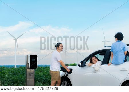Concept Of Progressive Happy Family Enjoying Their Time At Wind Farm With Electric Vehicle. Electric