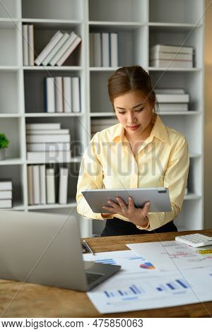 Concentered Female Economist Analyzing Financial Market On Digital Tablet While Standing At Her Work