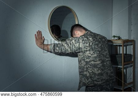Military Veteran With Mental Illness Standing Near Mirror At Home At Night.