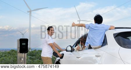 Concept Of Progressive Happy Family Enjoying Their Time At Wind Farm With Electric Vehicle. Electric