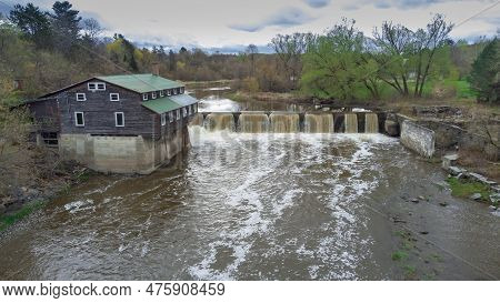 Old Water Mill Near A Waterfall In Spring On A Beautiful Riverin Quebec, Canada