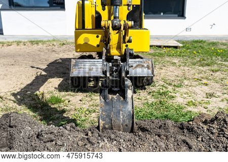 Mini Digger Digging A Hole In The Garden Along The Fence To The Drainage Pipes.