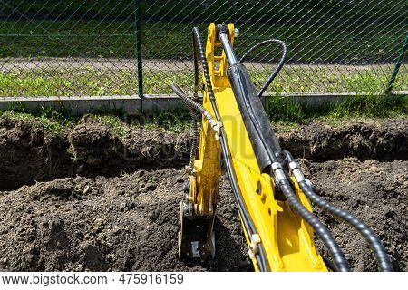 Mini Digger Digging A Hole In The Garden Along The Fence To The Drainage Pipes.