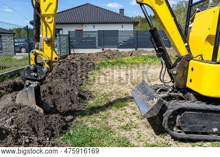 Mini Digger Digging A Hole In The Garden Along The Fence To The Drainage Pipes.