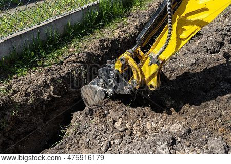 Mini Digger Digging A Hole In The Garden Along The Fence To The Drainage Pipes.