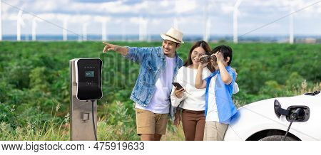 Concept Of Progressive Happy Family Enjoying Their Time At Wind Farm With Electric Vehicle. Electric