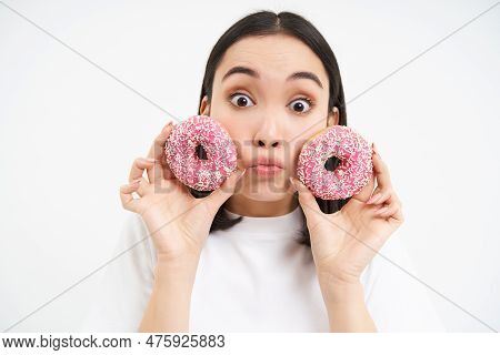 Portrait Of Funny Asian Woman, Tempted To Eat Tasty Glazed Dougnut, Holding Two Donnuts And Smiling 