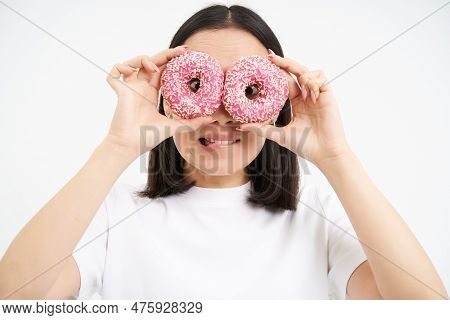 Image Of Funny Young Woman, Makes Glasses With Two Pink Glazed Doughnuts, Looking Through Donnut Hol