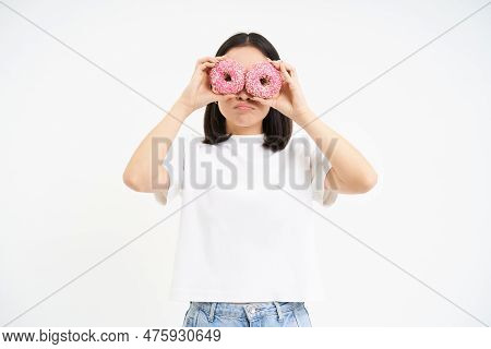 Image Of Funny Young Woman, Makes Glasses With Two Pink Glazed Doughnuts, Looking Through Donnut Hol