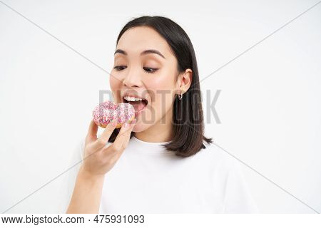 Close Up Of Smiling Pleased Asian Woman, Eats Glazed Pink Doughnut, Enjoys Eating Tasty Donnut, Whit
