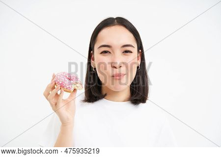 Close Up Of Smiling Pleased Asian Woman, Eats Glazed Pink Doughnut, Enjoys Eating Tasty Donnut, Whit