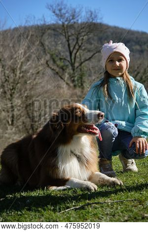 Children And Pets Concept. Charming Little Caucasian Girl Walks In Park With Her Dog. The Child Is S