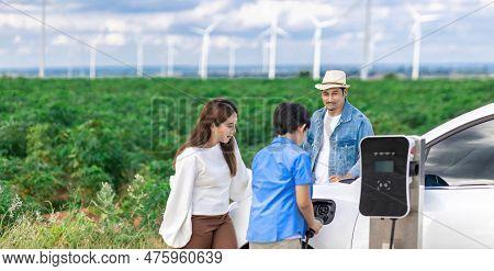Concept Of Progressive Happy Family Enjoying Their Time At Wind Farm With Electric Vehicle. Electric