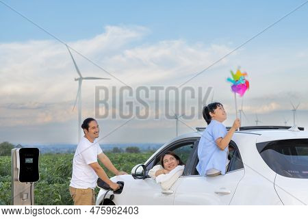 Concept Of Progressive Happy Family Enjoying Their Time At Wind Farm With Electric Vehicle. Electric