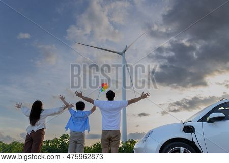 Concept Of Progressive Happy Family Enjoying Their Time At Wind Farm With Electric Vehicle. Electric