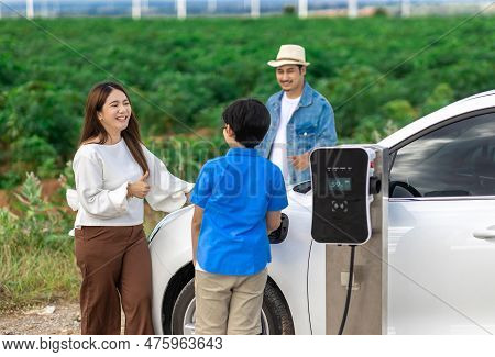 Concept Of Progressive Happy Family Enjoying Their Time At Wind Farm With Electric Vehicle. Electric