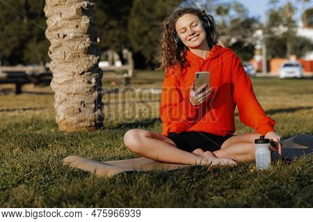 Young Smiling Sportswoman In Wirelles Headphones Listening Music And Using Cellphone During Workout 