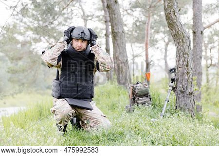 A Man In A Military Uniform And A Bulletproof Vest Works In The Forest To Demine The Territory. A Ma