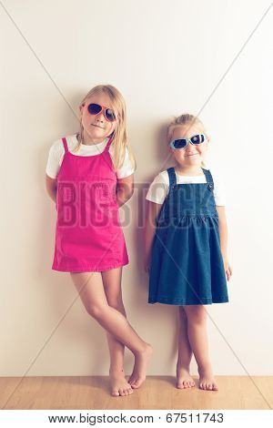 Two little girls posing in front of a walll. Studio shot.