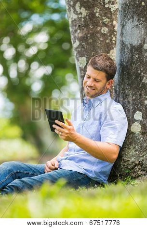 Young man reading E-Book outside in park