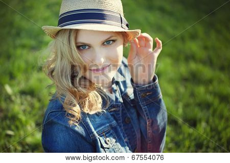 portrait of a beautiful young girl in a straw hat on a background of green grass