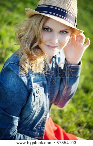 portrait of a beautiful young girl in a straw hat on a background of green grass