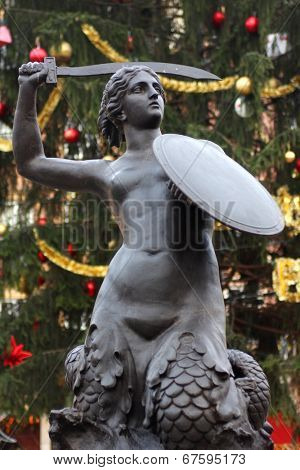 Syrenka statue in Old Town Market sqare in Warsaw with big Christmass tree in background. 