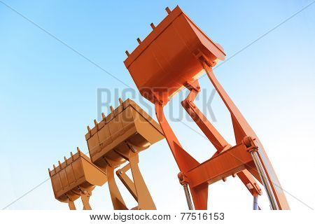 Part of  modern yellow excavator machines,the buckets/shovels raised against blue sky in a construction site.