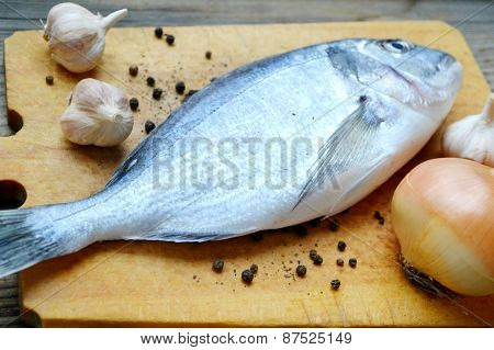 Uncooked fish dorado with garlic and onion