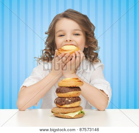 people, nutrition, childhood and health concept - happy little girl eating junk food over blue striped background