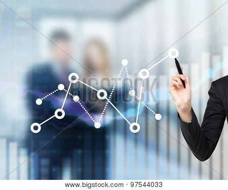 A Woman's Hand Is Drawing Fluctuation Of The Financial Chart. A Couple Of Colleagues On The Backgrou