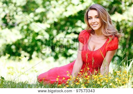 beautiful young woman in red dress sitting on grass