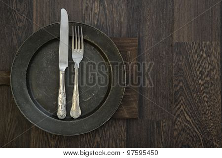 Pewter Plate And Vintage Cutlery On Rustic Dark Wooden Background