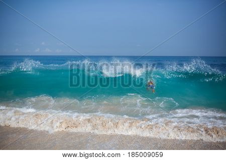 Horizontal panoramic photo of ocean waves and beach and the back side of a man who dives under the wave located on the right side of the frame.