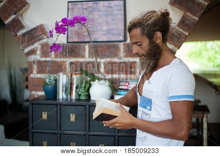 Portrait of trendy beard man standing near a book shelf in a cafe and reading a book