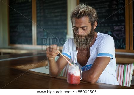 Attractive bearded curly man with a mug of smoothie is sitting in a cafe