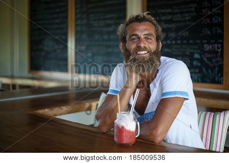 Attractive bearded curly man with a mug of smoothie is sitting in a cafe