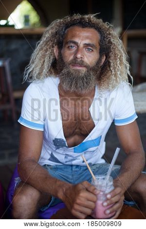 Attractive bearded curly man with a mug of smoothie is sitting in a cafe