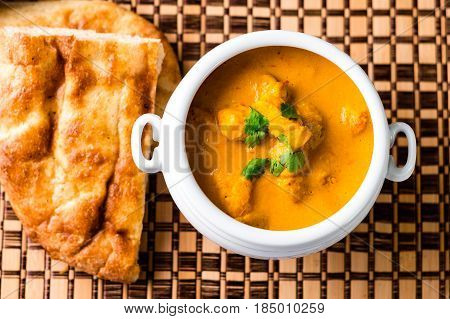 Butter chicken top view. Delicious butter chicken served in a white bowl with naan bread and rice on the side on a wooden place mat viewed from above.