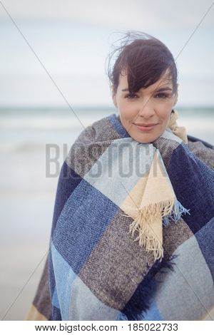Portrait of young woman with eays closed wrapped in blanket at beach during winter