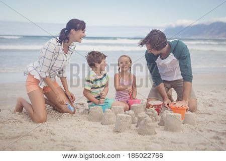 Happy siblings with parents making sand castle at beach