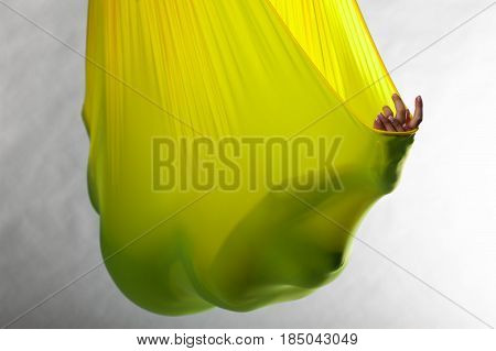 Unrecognized person lying in yellow hammock and meditating. Aerial yoga practice. Body balance and antigravity training. Wellness and body care concept.