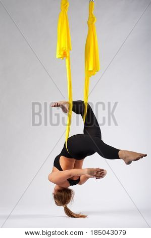 Young flexible girl working out in yellow hammock. Blonde woman practicing fly yoga or aerial acrobatics, studio shot. Body balance and antigravity training. Wellness and body care concept.