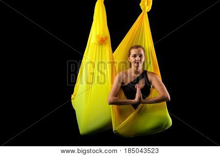 Young relaxed yogi woman meditating in yellow hammock. Blonde girl practicing aerial yoga, studio shot. Body balance and antigravity exercises. Wellness and bodycare concept