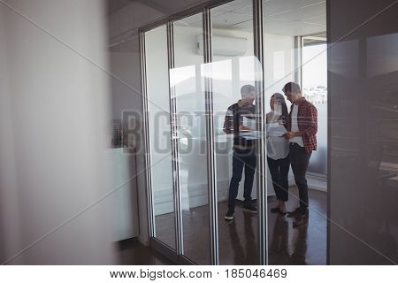 Young business colleagues dicussing over documets at office seen through glass